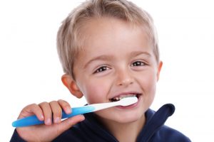 Smiling child brushing teeth with blue toothbrush.